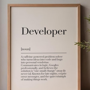 May include: A framed print with a light beige background and a wooden frame. The print features the word "Developer" in bold black font, followed by a definition. The definition describes a problem solver who turns ideas into code.
