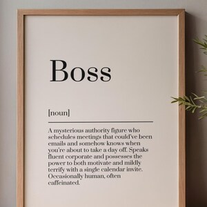 Peut inclure: Impression encadrée avec le mot « Boss » en grosses lettres noires. En dessous, une définition décrit une mystérieuse figure d'autorité. Le cadre est de couleur marron clair et le fond est beige neutre.