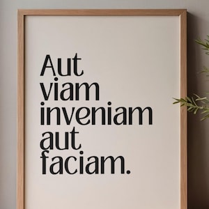 May include: A framed print with the Latin phrase "Aut viam inveniam aut faciam" in bold black letters. The print has a cream-colored background and is encased in a light brown wooden frame. The artwork is displayed on a wooden surface.