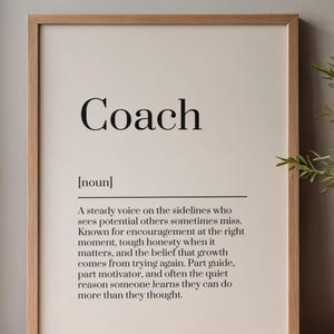Może przedstawiać: Oprawiony wydruk z napisem "Coach" pogrubioną czcionką. Poniżej definicja opisuje trenera jako stały głos, oferujący zachętę i uczciwość. Rama jest w kolorze jasnobrązowym.