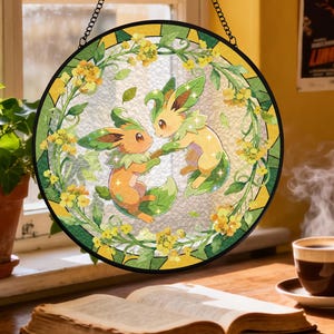 Może przedstawiać: Okrągłe witraż przedstawiający dwie postacie z kreskówek z zielonym i pomarańczowym futrem, otoczone żółtymi kwiatami i zielonymi liśćmi. Okno jest oprawione w czarną ramę i zawieszone na łańcuchu.