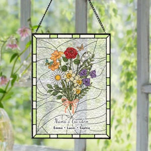 May include: Stained glass panel featuring a colorful floral bouquet with a red rose, orange flowers, and daisies. The panel is framed in black and green, with the text "Nana's Garden" and names below. Includes butterflies.