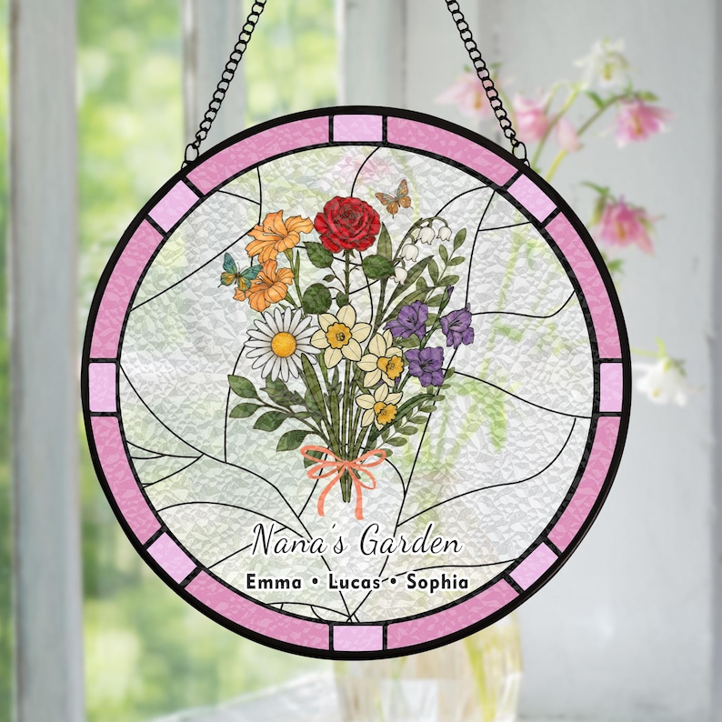 May include: Round stained glass window with a pink border and a black chain for hanging. The window features a bouquet of flowers, butterflies, and the text "Nana's Garden" with names below.