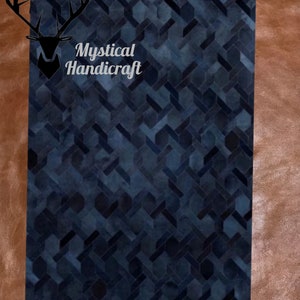 May include: A dark blue, geometric patterned rug with the text "Mystical Handicraft" in white. The rug has a herringbone design and is set against a brown leather background.