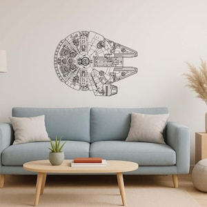 May include: A black and white wall art piece depicting the Millennium Falcon spaceship. The artwork is mounted on a white wall above a light blue sofa. The room is decorated with neutral-toned furniture and decor.