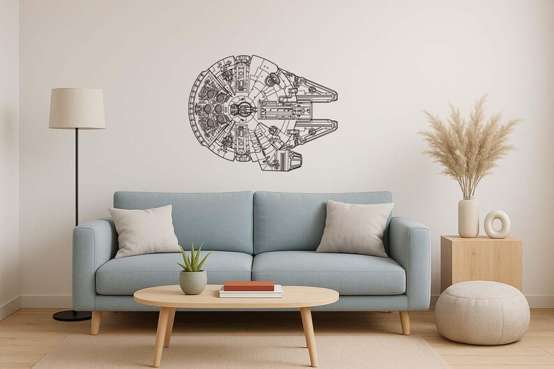 May include: A black and white wall art piece depicting the Millennium Falcon spaceship. The artwork is mounted on a white wall above a light blue sofa. The room is decorated with neutral-toned furniture and decor.