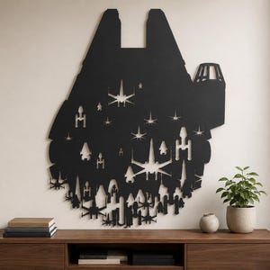 May include: A large, matte black wall art piece shaped like the Millennium Falcon starship. The silhouette features intricate cutouts of various starfighters and spacecraft from the Star Wars universe, creating a detailed negative space design.