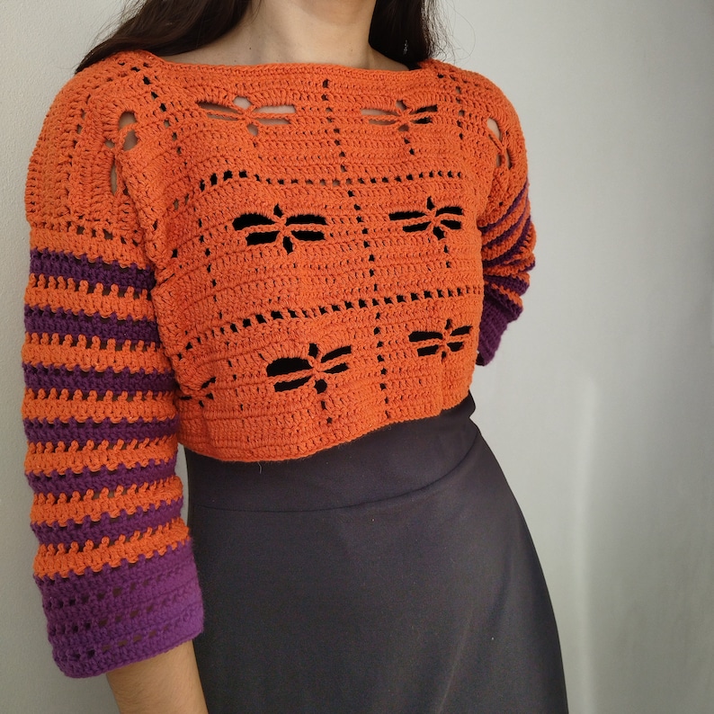 Puede incluir: Un su&eacute;ter de crochet naranja recortado con una manga a rayas de color morado y naranja. El su&eacute;ter tiene un patr&oacute;n geom&eacute;trico con formas de lib&eacute;lula.