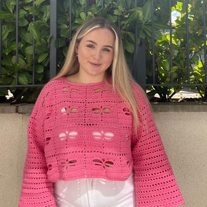 Puede incluir: Un su&eacute;ter de crochet rosa de corte holgado y un delicado patr&oacute;n de calado. El su&eacute;ter tiene mangas largas y una longitud recortada.