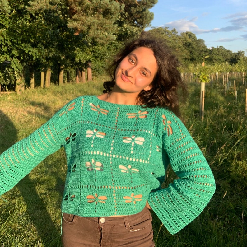 Puede incluir: Un su&eacute;ter de crochet verde con un dise&ntilde;o de lib&eacute;lula blanca. El su&eacute;ter tiene una longitud recortada y mangas largas.