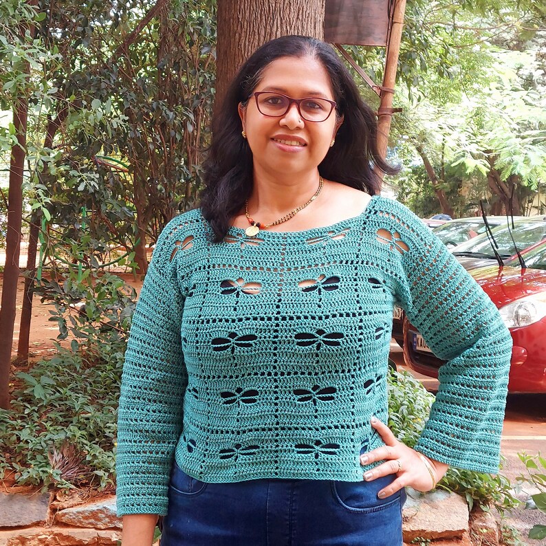 Puede incluir: Un top de crochet de color turquesa con un dise&ntilde;o de lib&eacute;lula. El top tiene un escote redondo y mangas largas.