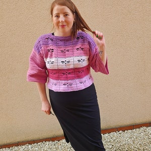 Puede incluir: Un top de crochet a rayas rosa, morado y blanco, de corte holgado y mangas acampanadas.