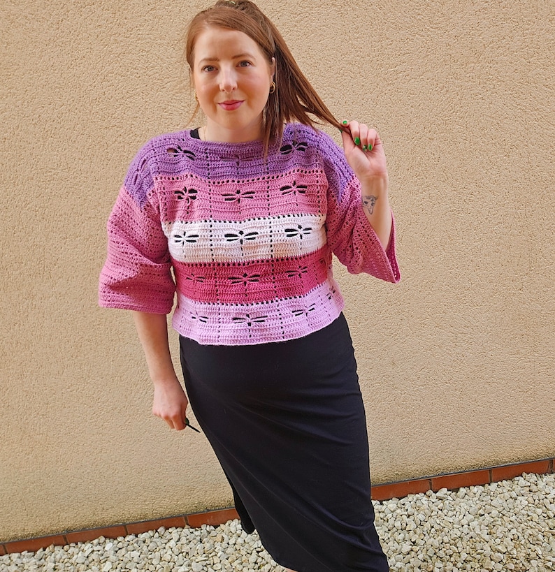 Puede incluir: Un top de crochet a rayas rosa, morado y blanco, de corte holgado y mangas acampanadas.