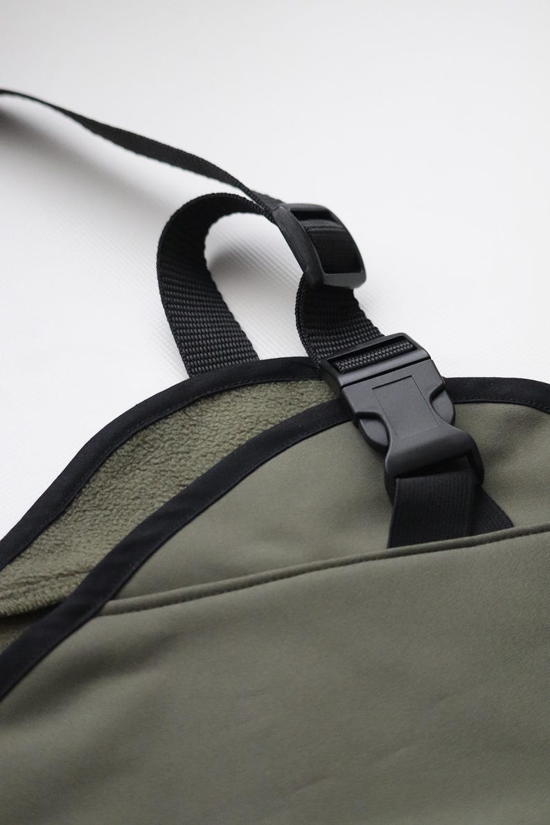 Pu&ograve; includere: Primo piano di un oggetto in tessuto verde con finiture e cinghie nere. &Egrave; visibile una fibbia in plastica nera, insieme a una cinghia nera. L'oggetto ha una morbida fodera interna strutturata. Lo sfondo &egrave; bianco.