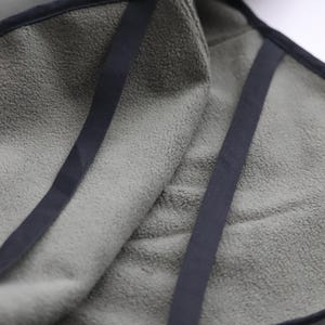 Pu&ograve; includere: Primo piano di un asciugamano verde oliva piegato con finiture e cinghie blu navy scuro. L'asciugamano ha un aspetto morbido e strutturato. Le cinghie sono cucite sull'asciugamano, creando un aspetto pulito e rifinito. L'asciugamano &egrave; piegato su se stesso.