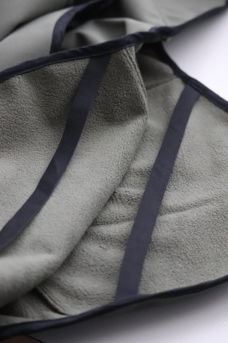 Pu&ograve; includere: Primo piano di un asciugamano verde oliva piegato con finiture e cinghie blu navy scuro. L'asciugamano ha un aspetto morbido e strutturato. Le cinghie sono cucite sull'asciugamano, creando un aspetto pulito e rifinito. L'asciugamano &egrave; piegato su se stesso.