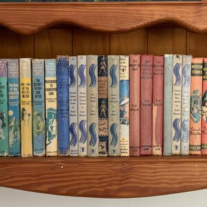 May include: A shelf full of vintage paperback books with colorful covers. The books are organized by color and feature titles like "The Mystery of the Whispering  Well" and "The Mystery of the Hidden  Room".