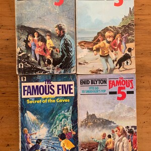 May include: Four paperback books with colorful covers featuring illustrations of children and dogs. The books are all part of the "Famous Five" series by Enid Blyton. The titles are "Five Go Off in a Caravan", "Five on a Treasure Island", "The Famous Five and the Secret of the Caves", and "Five Go to Smuggler's Top".