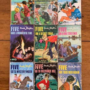 May include: A collection of nine paperback books with colorful covers featuring illustrations of children and animals. The books are titled "Five" and each book has a different subtitle. The books are part of the "Famous Five" series by Enid Blyton.