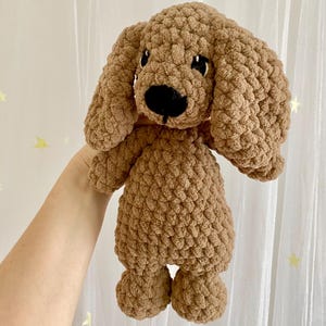 May include: A brown crocheted stuffed dog toy with black eyes and a black nose. The dog is standing on its four legs and has floppy ears.