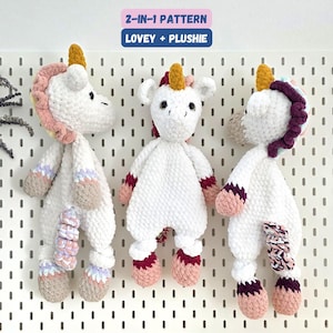 Puede incluir: Tres peluches de unicornio de ganchillo hechos a mano en blanco, con crines, cuernos y cascos coloridos. El texto "2-IN-1 PATTERN LOVEY + PLUSHIE" está en la parte superior. Los unicornios tienen detalles en rosa, morado y burdeos.