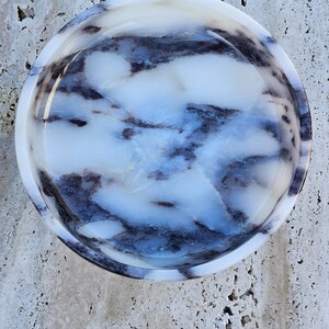 May include: A round, white marble bowl with a swirling blue and black pattern. The bowl is smooth and polished.