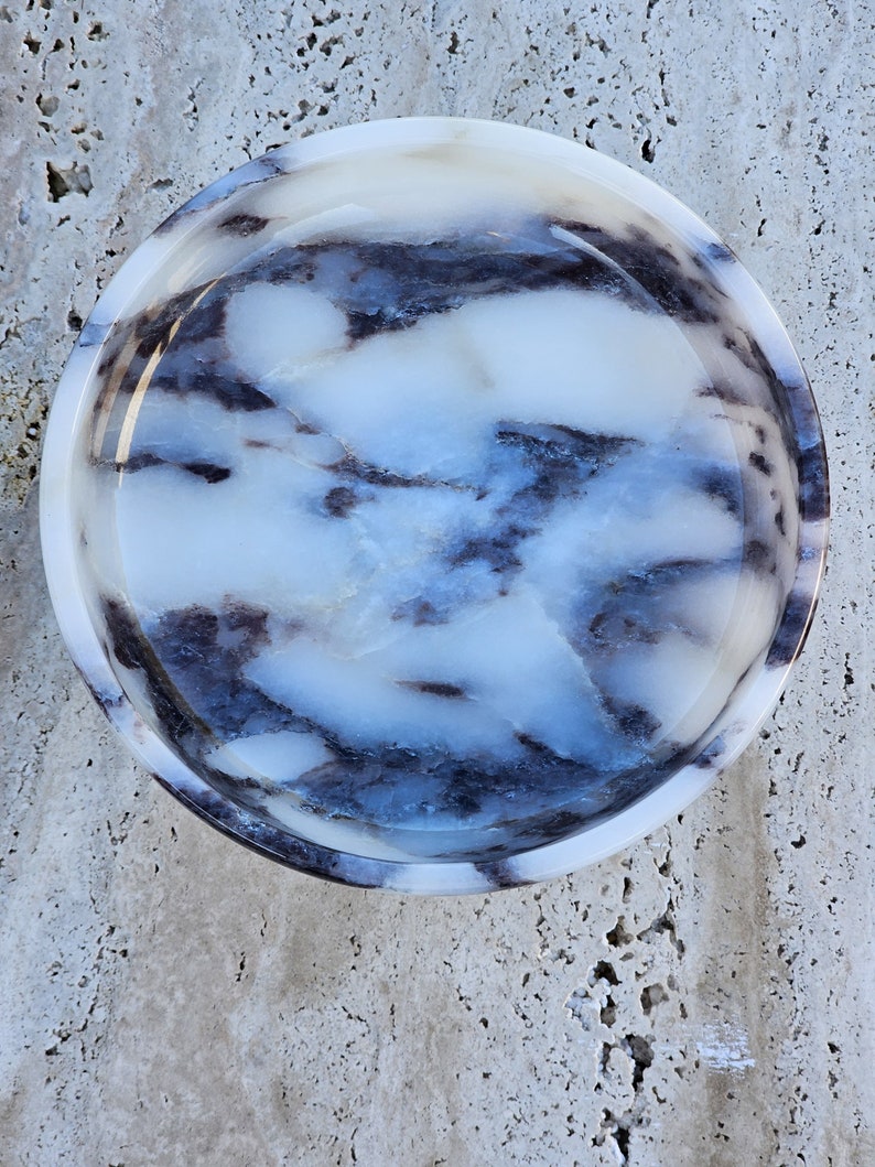 May include: A round, white marble bowl with a swirling blue and black pattern. The bowl is smooth and polished.