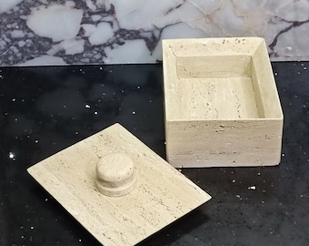 Op de afbeelding: Een beige travertijnstenen doos met een deksel. Het deksel heeft een ronde knop bovenop. De doos is open en de binnenkant is leeg.
