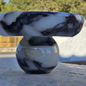 May include: A white and black marble bowl with a round base. The bowl is made of alabaster and has a unique marbled pattern.