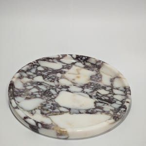 Puede incluir: Bandeja redonda de mármol con base blanca y patrón de remolino púrpura y dorado.