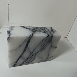 Può includere: Un blocco di marmo bianco con venature grigio scuro. La scultura rettangolare ha un lato inclinato, che le conferisce una forma geometrica unica. La pietra naturale presenta una finitura lucida, che mette in risalto gli intricati motivi.