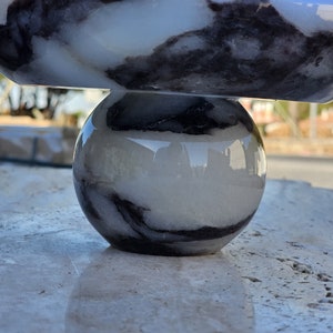 May include: A white and black marble bowl sits on top of a white and black marble sphere. Both pieces are smooth and polished.