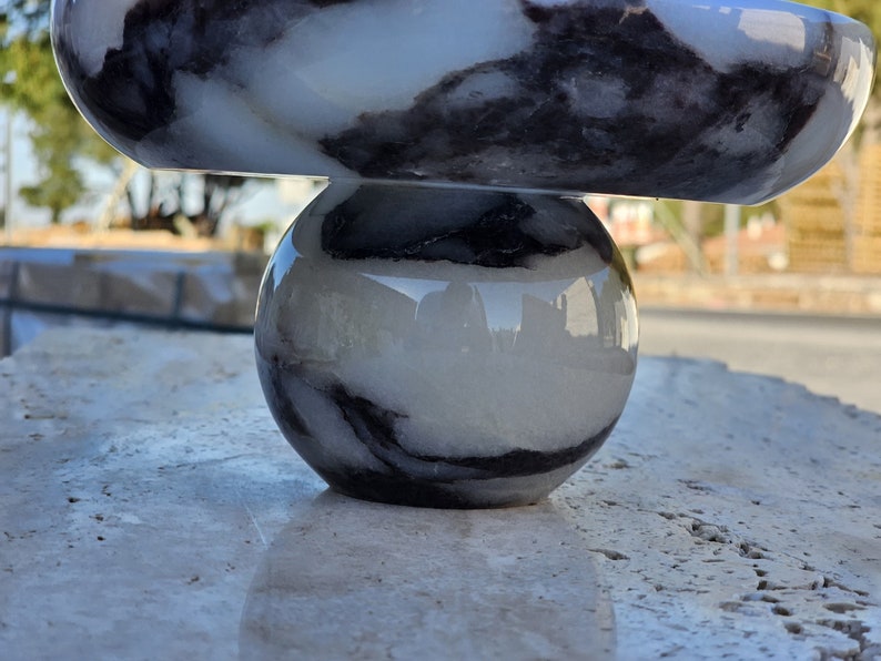 May include: A white and black marble bowl sits on top of a white and black marble sphere. Both pieces are smooth and polished.