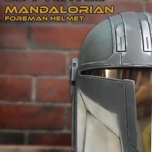 May include: A 3D printed Mandalorian Foreman helmet featuring a weathered dark gray finish with lighter gray accents and a metallic visor. The text 3D PRINTED MANDALORIAN FOREMAN HELMET is displayed above the helmet in a bold, stylized font.