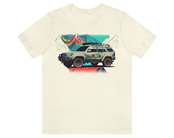 Op de afbeelding: Een wit T-shirt met een kleurrijke illustratie van een groene SUV met een dakdrager die door een berglandschap rijdt. De bergen zijn geschilderd in tinten rood, oranje, geel, groen en blauw.