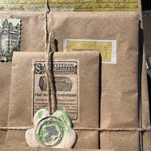 Puede incluir: Un montón de paquetes de papel marrón atados con hilo, adornados con cinta decorativa, sellos y un sello de cera. Los paquetes presentan etiquetas y texto vintage, incluyendo "PICCADILLY CIRCUS" y "S. DELABARRE NARCOTIQUE".