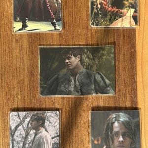Puede incluir: Conjunto de cinco cromos con im&aacute;genes de un hombre con varios trajes. Las tarjetas muestran al hombre en diferentes escenarios, incluyendo una actuaci&oacute;n, al aire libre y primeros planos. Las tarjetas se muestran sobre una superficie de madera.