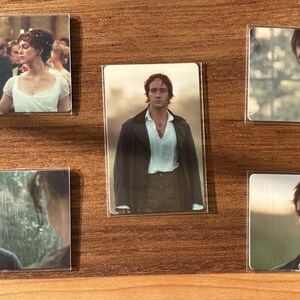Puede incluir: Un conjunto de cinco imanes rectangulares con im&aacute;genes de actores con trajes de &eacute;poca, sobre un fondo de madera. Los imanes muestran escenas de un drama hist&oacute;rico, con retratos de personajes.