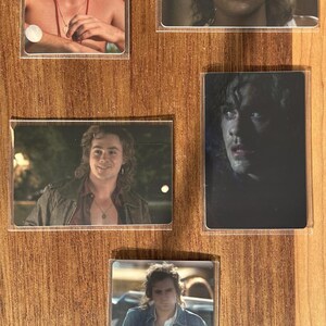 Puede incluir: Juego de cinco cromos con un hombre de pelo largo y ondulado. Los cromos muestran diferentes im&aacute;genes del hombre, incluyendo una con fondo rojo y otra con chaqueta vaquera. Los cromos est&aacute;n en fundas protectoras.