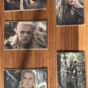 Puede incluir: Conjunto de cinco tarjetas rectangulares con im&aacute;genes de un personaje con pelo largo y rubio de una pel&iacute;cula de fantas&iacute;a. Las tarjetas se muestran sobre una superficie de madera. El personaje lleva varios trajes y sostiene un arco y una flecha en algunas im&aacute;genes.