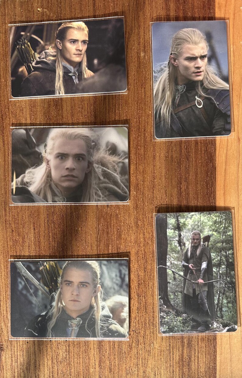 Puede incluir: Conjunto de cinco tarjetas rectangulares con im&aacute;genes de un personaje con pelo largo y rubio de una pel&iacute;cula de fantas&iacute;a. Las tarjetas se muestran sobre una superficie de madera. El personaje lleva varios trajes y sostiene un arco y una flecha en algunas im&aacute;genes.