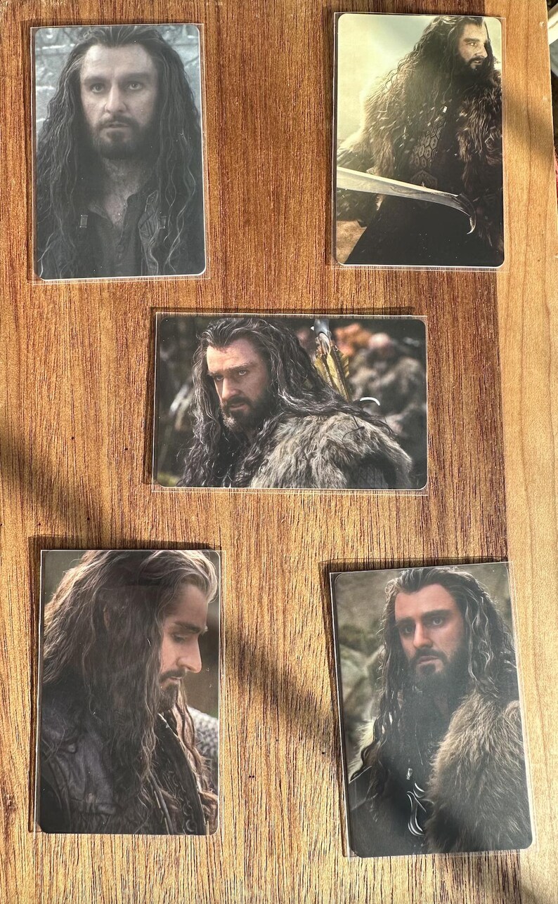Puede incluir: Conjunto de cinco cromos que muestran a un hombre con pelo largo y ondulado y barba. Los cromos muestran diferentes poses, algunas con una espada o ropa con forro de piel. Los cromos se presentan sobre una superficie de madera.