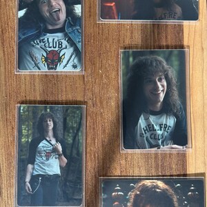 Puede incluir: Una colecci&oacute;n de cinco tarjetas rectangulares con im&aacute;genes de una persona con cabello largo y rizado. Las tarjetas muestran a la persona usando camisas con el texto "HELLFIRE CLUB" y "CLUB". El fondo es una superficie de madera.