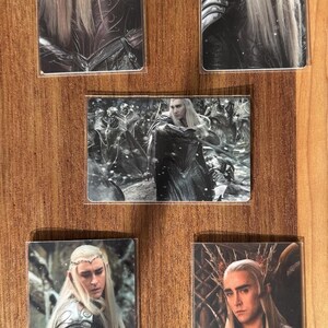 Puede incluir: Conjunto de cinco cromos que representan a un personaje con pelo largo y rubio y rasgos &eacute;lficos. Los cromos muestran al personaje en diferentes escenas, vistiendo armadura y ropa regia. El fondo es una superficie de madera.