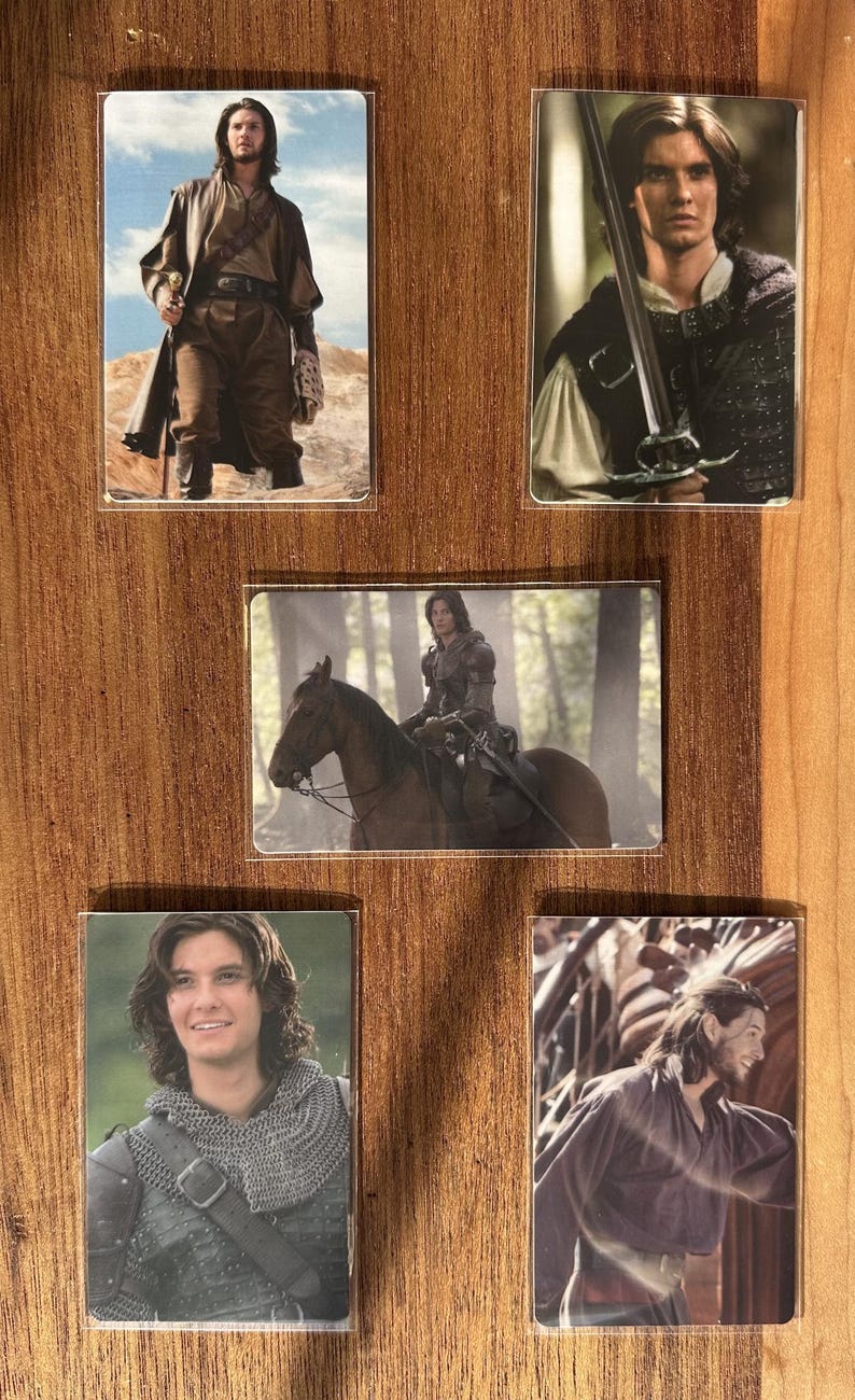 Puede incluir: Conjunto de cinco tarjetas rectangulares en fundas transparentes, con im&aacute;genes de un hombre con diferentes trajes. Las im&aacute;genes muestran al hombre en escenarios medievales o fant&aacute;sticos, con espadas y montando a caballo.