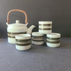 May include: A white teapot with a brown bamboo handle and brown stripes, and four matching white teacups with brown stripes.
