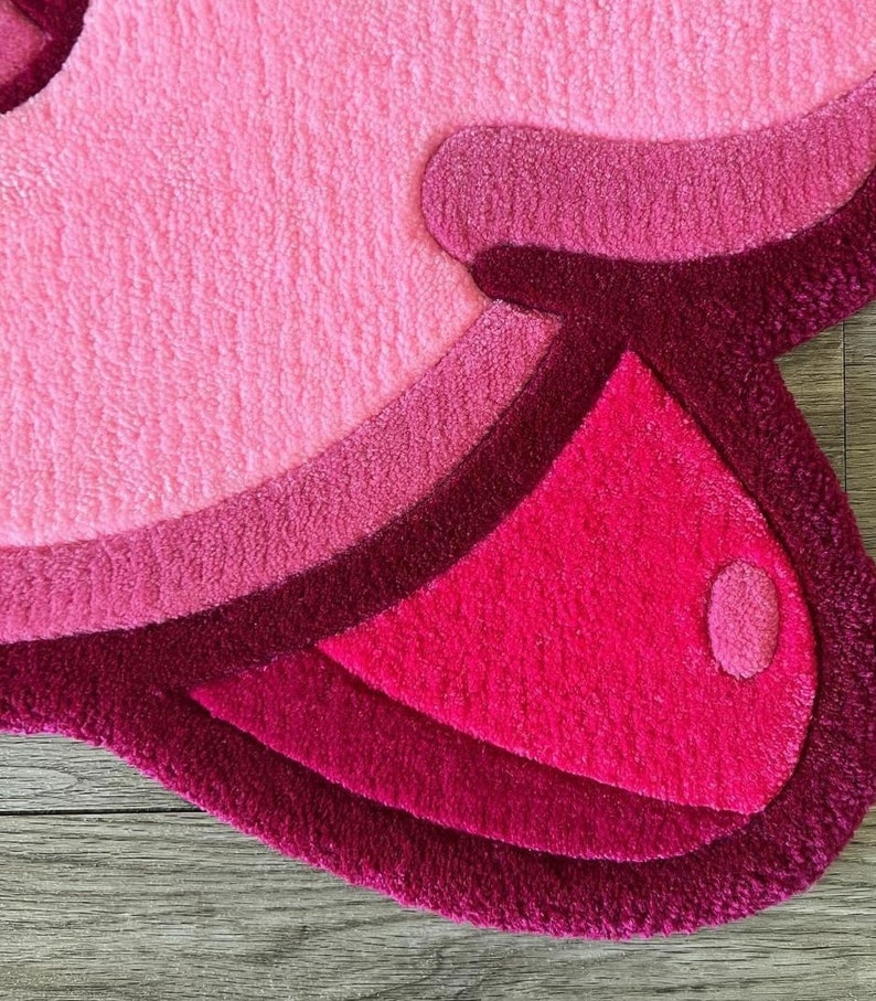 Puede incluir: Una alfombra peluda rosa y roja con un dise&ntilde;o ondulado. La alfombra tiene forma de nube y una textura suave y mullida.
