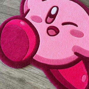 Puede incluir: Alfombra de felpa rosa y roja con forma de personaje de dibujos animados con un ojo gui&ntilde;ando y una mejilla grande, redonda y rosa.