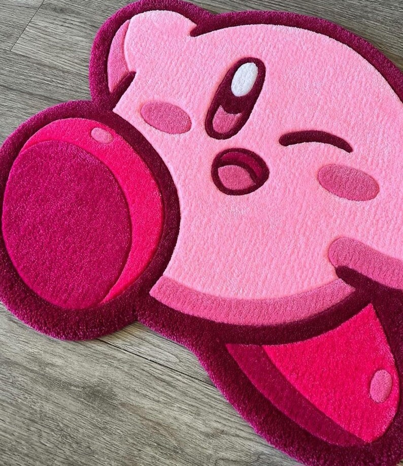 Puede incluir: Alfombra de felpa rosa y roja con forma de personaje de dibujos animados con un ojo gui&ntilde;ando y una mejilla grande, redonda y rosa.