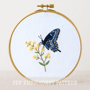 May include: Embroidered butterfly and yellow flowers on white fabric, set in a gold hoop. The butterfly is navy blue with orange accents. The text "PDF EMBROIDERY PATTERN" is at the bottom.